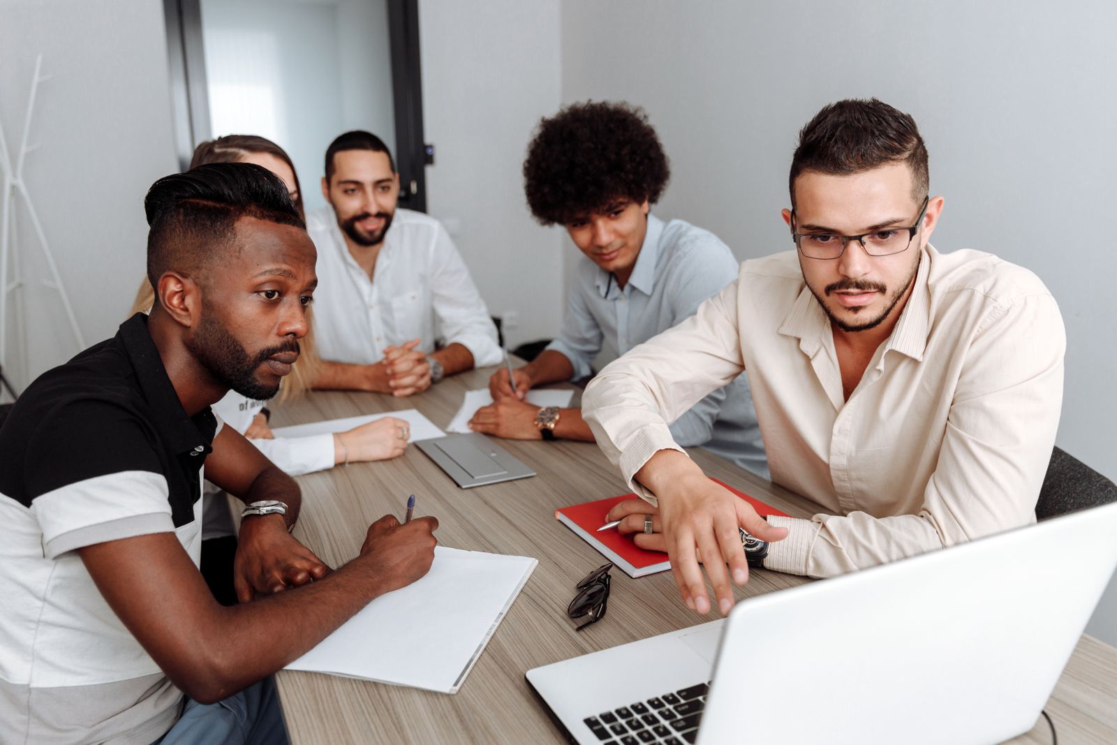 Diverse team of five colleagues gathered around a laptop in a shared workspace, collaborating on documents