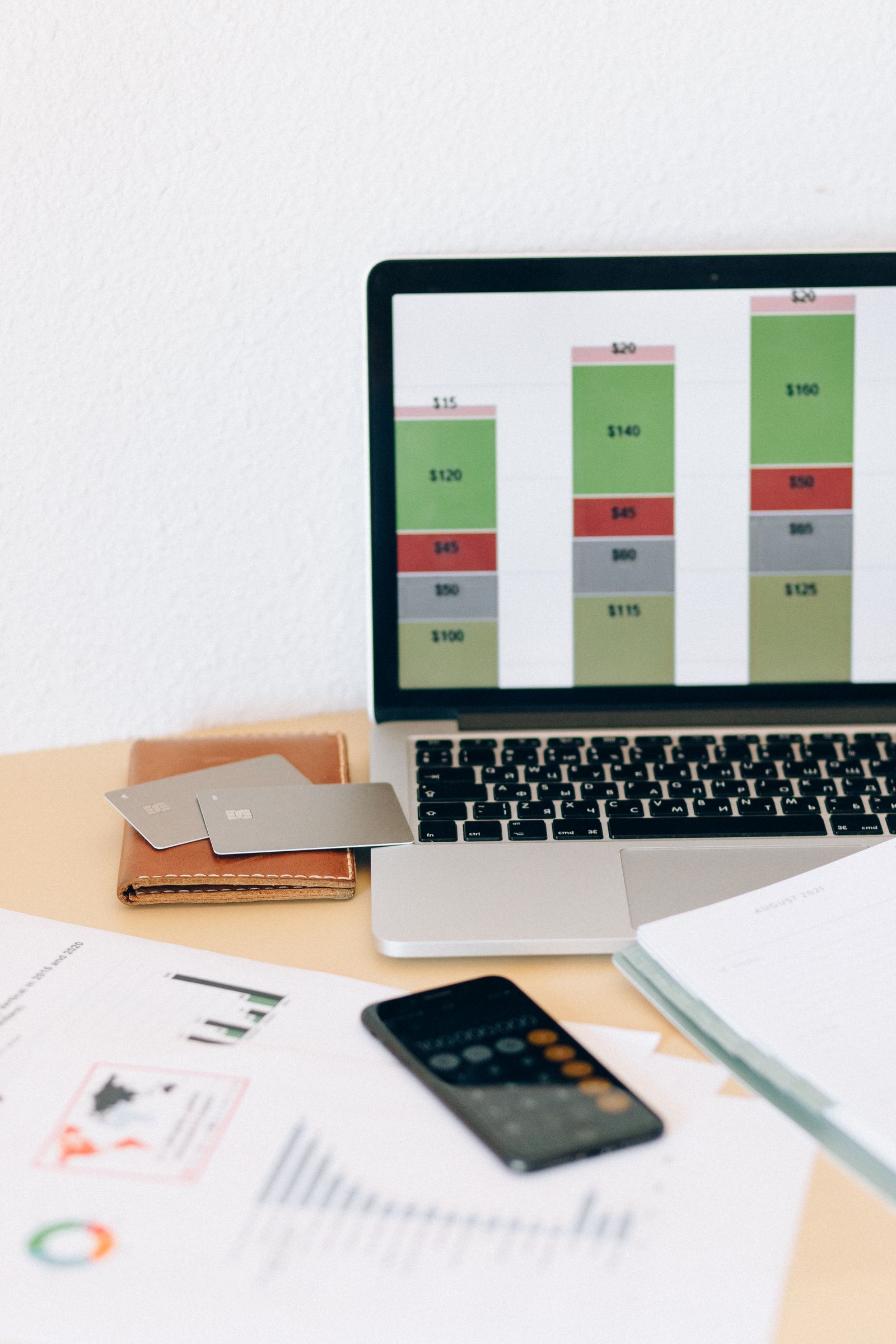 Laptop showing an accounts payable expense breakdown with printed reports and a mobile calculator on the desk